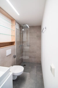 Schmales vorgefertigtes Badezimmer mit Walk-in-Dusche, grauen Fliesen und Wand-WC.