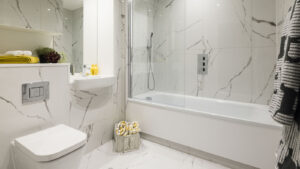 Weißes Badezimmer mit Marmorfliesen, Badewanne mit Duschwand und Wand-WC.