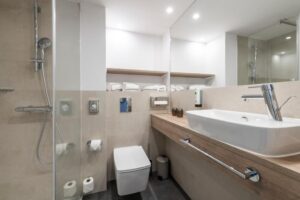 Badezimmer mit beigen Fliesen, Walk-in-Dusche, Holzwaschtisch mit Aufsatzbecken und Spiegel.