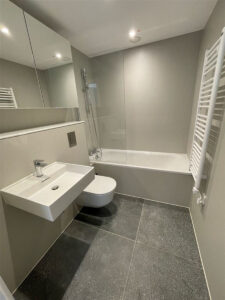 Graues Badezimmer mit Badewanne und Dusche, Wand-WC, Waschbecken und weißem Handtuchheizkörper.