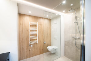 Badezimmer mit Holzoptik-Wand, schwarzem Waschtisch und großem beleuchtetem Spiegel.