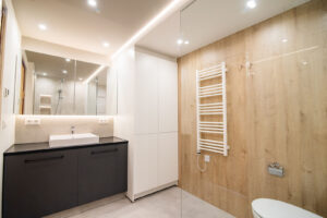 Walk-in-Dusche mit Regenbrause, beigen Fliesen in Steinoptik, Wandnischen und Wand-WC.