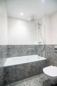 Badezimmer mit Badewanne und Regenbrause, in grauem Terrazzo, mit Wand-WC.