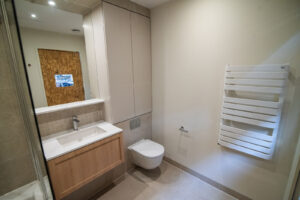 Badezimmer mit Holznische, weißem Waschtisch, Wand-WC und Walk-in-Dusche.