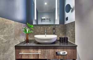 Badezimmer mit Aufsatzwaschbecken auf Holzwaschtisch, großem Spiegel und Mosaikwand.