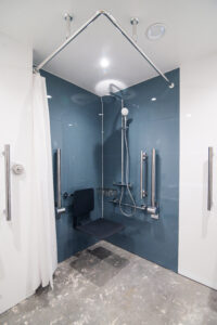 Barrierefreier Duschbereich mit Haltegriffen, Klappsitz und blauer Wandverkleidung.