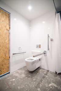Barrierefreies Badezimmer mit Wand-WC, Haltegriffen für Menschen mit Behinderung und OSB-Tür.