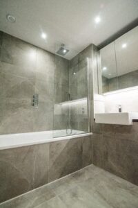 Graues Badezimmer mit Badewanne und Dusche, Spiegelschrank und Fliesen in Steinoptik.