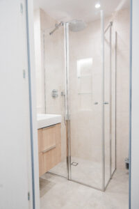 Badezimmer mit Duschkabine, Holzwaschtisch und beigen Fliesen.
