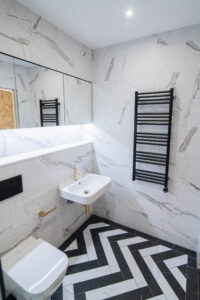 Elegantes Badezimmer mit Marmorfliesen, schwarzem Heizkörper und schwarz-weißem Fischgrätboden.