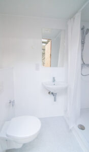 Weißes Badezimmer mit Dusche hinter Vorhang, Wandwaschbecken und Wand-WC.