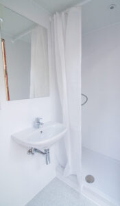 Weißes Badezimmer mit Waschbecken, Spiegel und Dusche hinter Vorhang.