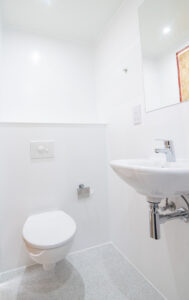Weißes Badezimmer mit Wand-WC, Wandwaschbecken und Spiegel.