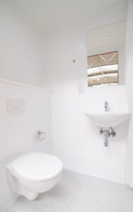 Weißes Badezimmer mit Wand-WC, Waschbecken und Fenster.
