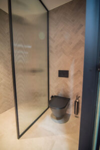 Badezimmer mit Fischgrätfliesen, schwarzer Duschtrennwand und schwarzem Wand-WC.