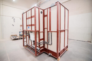 Vorgefertigtes Badmodul auf rotem Rahmen mit kompletter Wasser- und Abwasserinstallation.