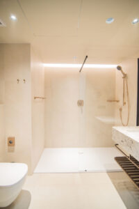 Beiges Badezimmer mit Walk-in-Dusche, Wand-WC, Waschbecken und LED-Beleuchtung.