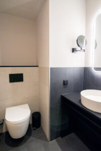 Zweifarbiges Badezimmer mit schwarzem Waschtisch, rundem Spiegel und Wand-WC.
