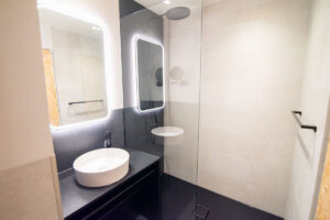 Badezimmer mit beleuchteten Spiegeln, Aufsatzwaschbecken auf schwarzem Unterschrank und Walk-in-Dusche.