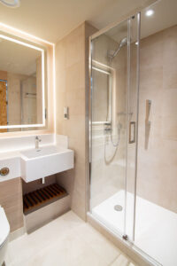 Beiges Badezimmer mit beleuchtetem Spiegel, Waschbecken und Duschkabine.