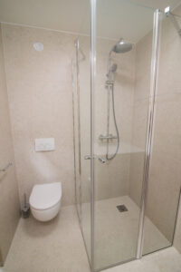 Beiges Badezimmer mit Walk-in-Dusche samt Regenbrause und Wand-WC.